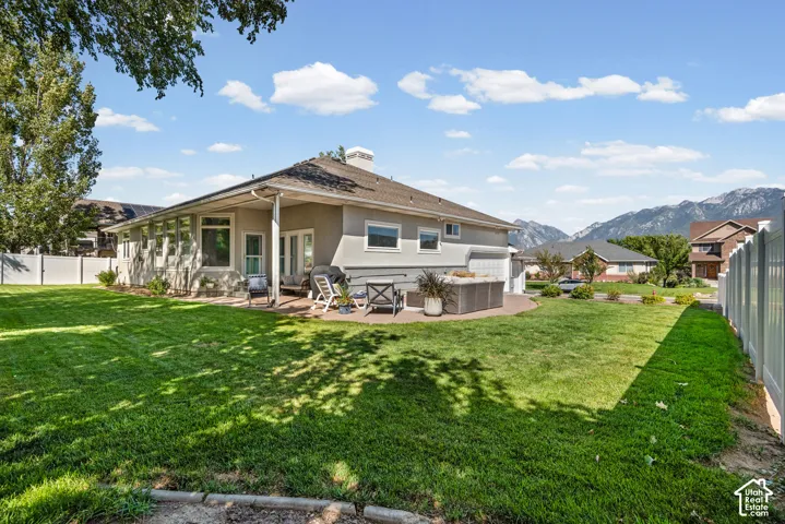 Expansive backyard featuring a manicured lawn, stucco exterior, multiple windows, and a paved patio area