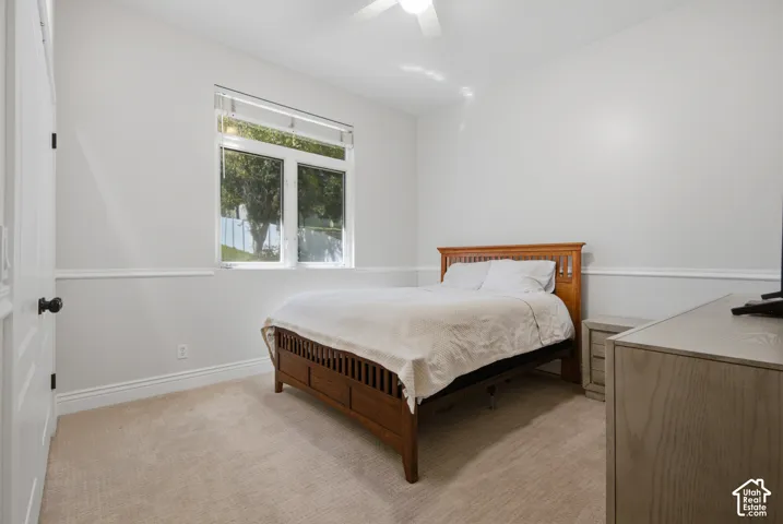 Light-colored carpeting, a window with horizontal blinds, and a ceiling fan with integrated lighting