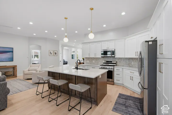 Open-concept kitchen featuring an island with a light-toned countertop, white cabinetry with silver hardware, stainless steel appliances, and wood-finish flooring