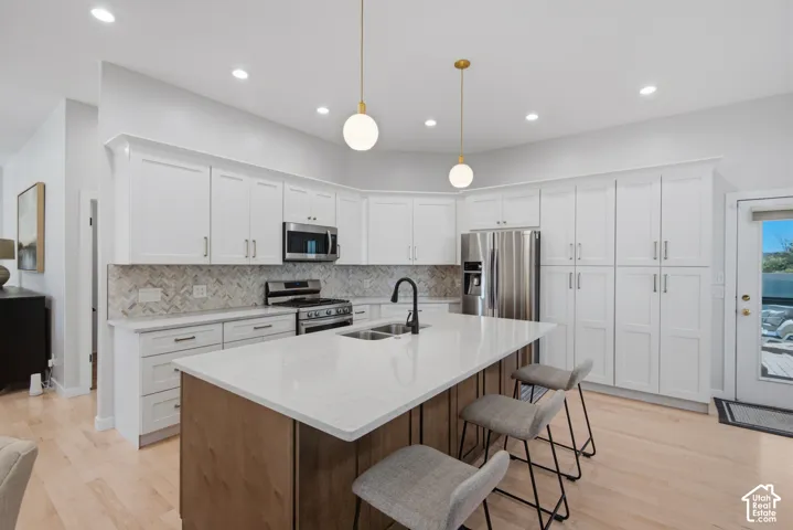 White shaker cabinetry, stainless steel appliances, stone countertops, herringbone tile backsplash, and light wood-finish flooring