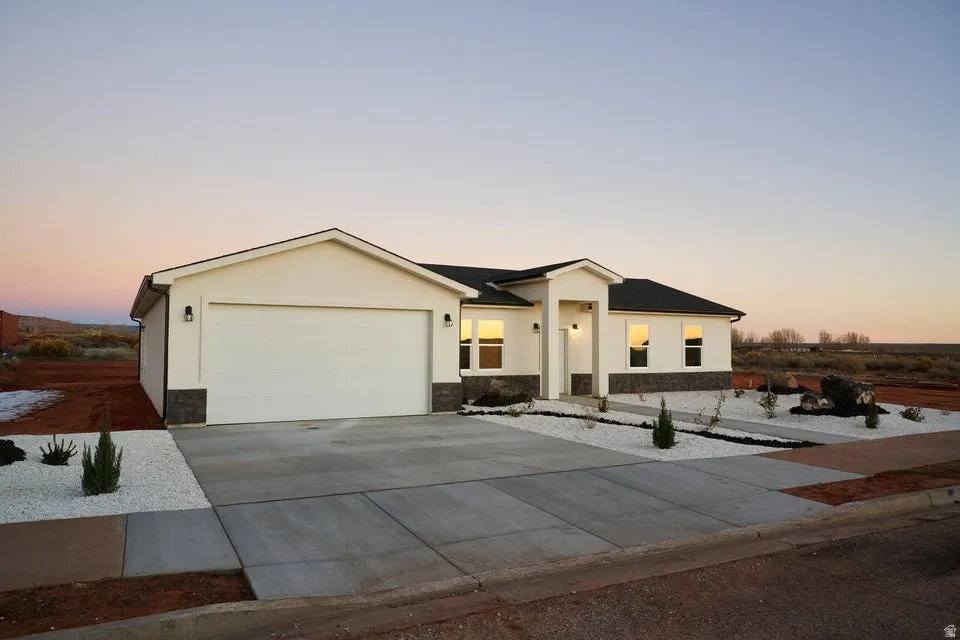 View of front facade featuring driveway, stone siding, a garage, and stucco siding