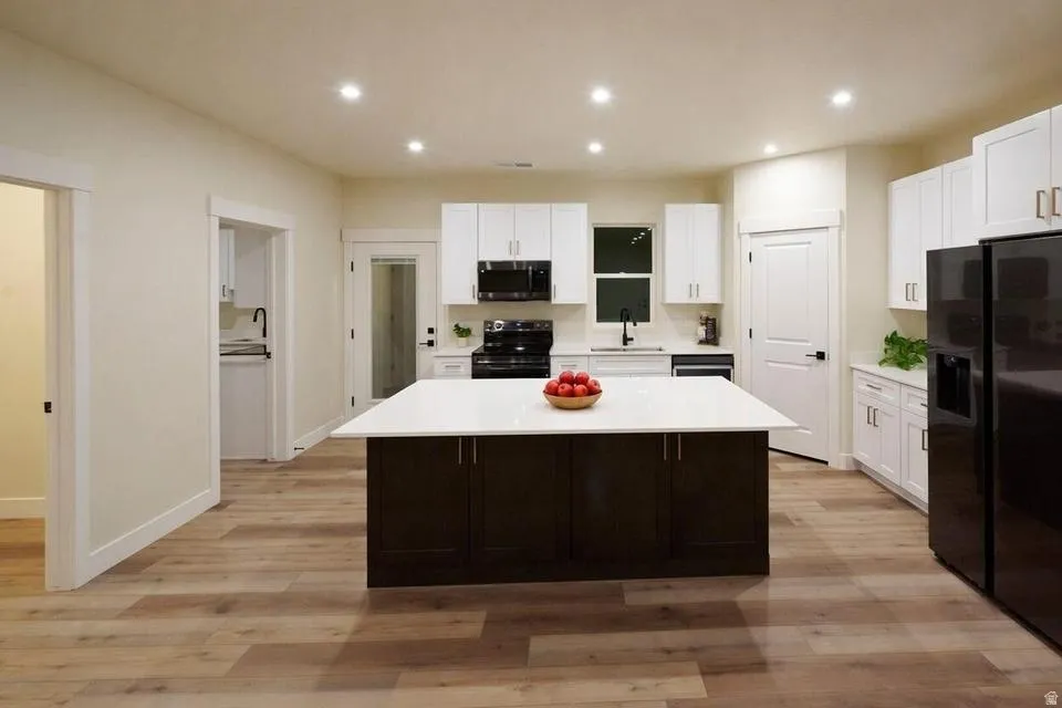 Two tone kitchen featuring black appliances, dual tone cabinetry, a center island, light wood finished floors, and recessed lighting