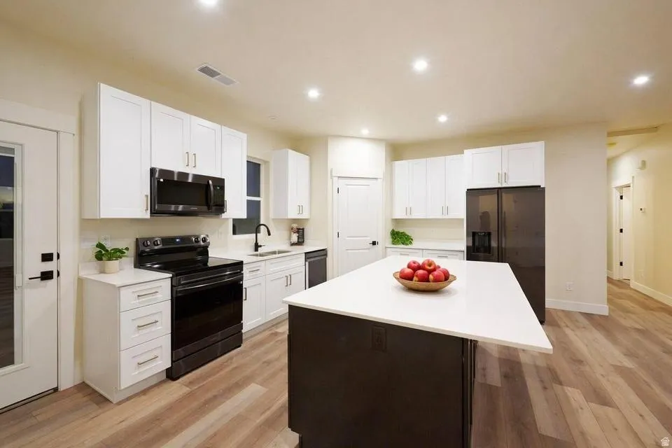 Kitchen featuring a center island, black appliances, two tone cabinets, light wood-type flooring, and recessed lighting