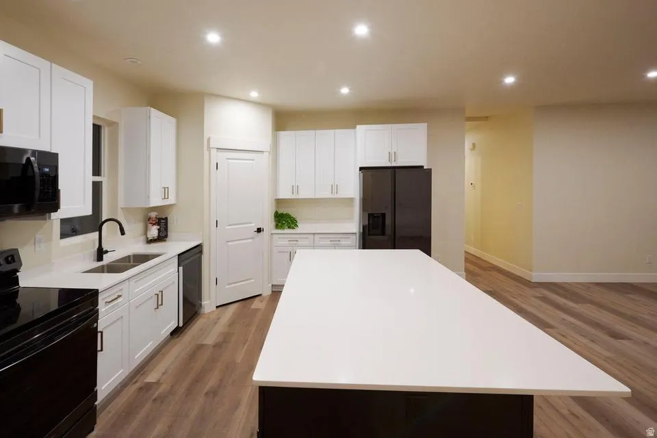 Kitchen featuring black appliances, a kitchen island, light wood-type flooring, white cabinets, and recessed lighting
