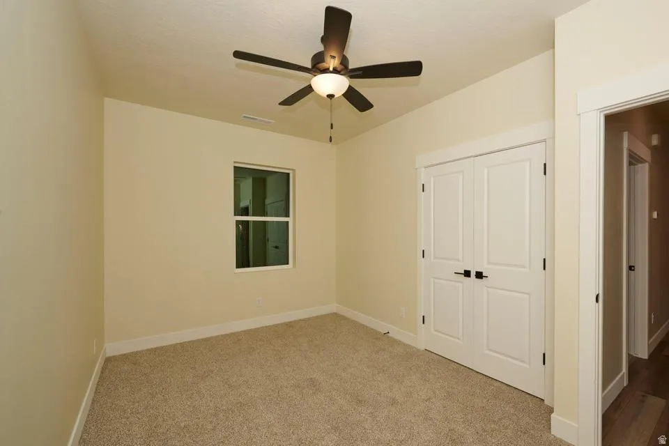 Unfurnished bedroom featuring light carpet, a closet, and ceiling fan