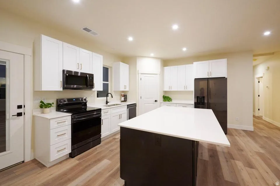Kitchen featuring a kitchen island, black appliances, light wood-style flooring, recessed lighting, and dual tone cabinets