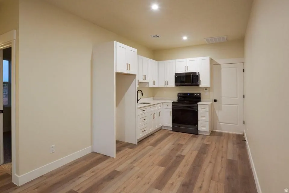 Kitchen with white cabinets, black electric range, light countertops, light wood-style floors, and recessed lighting