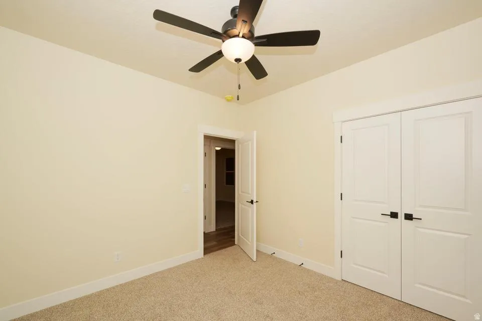 Unfurnished bedroom featuring light colored carpet, a closet, and ceiling fan