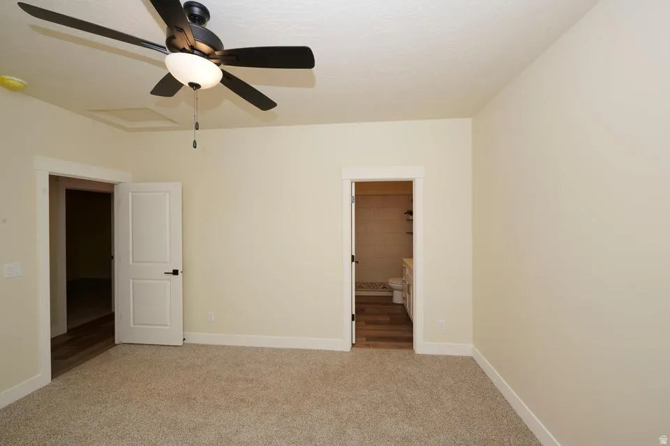Unfurnished bedroom featuring light colored carpet, ensuite bathroom, and a ceiling fan