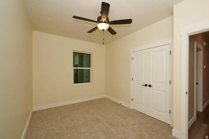 Unfurnished bedroom featuring light carpet, a closet, and ceiling fan