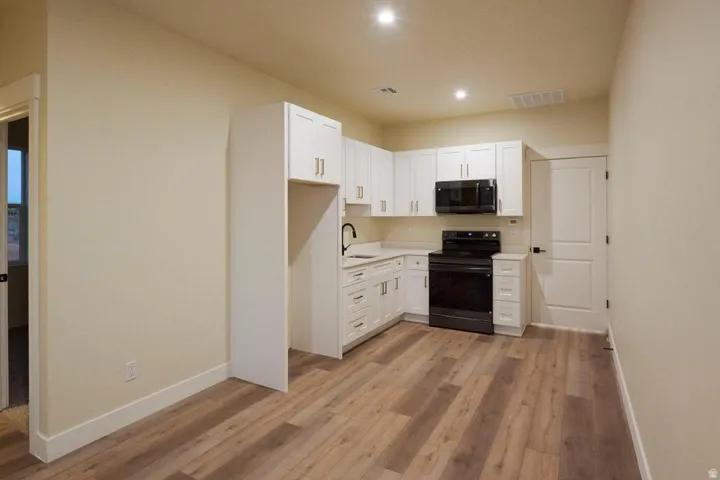 Kitchen with white cabinets, black electric range, light countertops, light wood-style floors, and recessed lighting