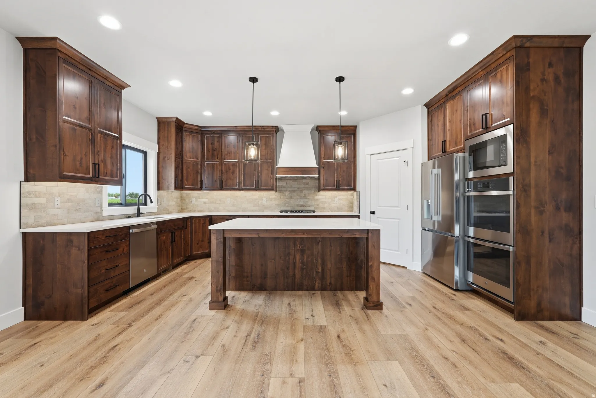 Kitchen featuring dark wood finish cabinets, stainless steel appliances, a center island, pendant lighting, and light wood finished floors