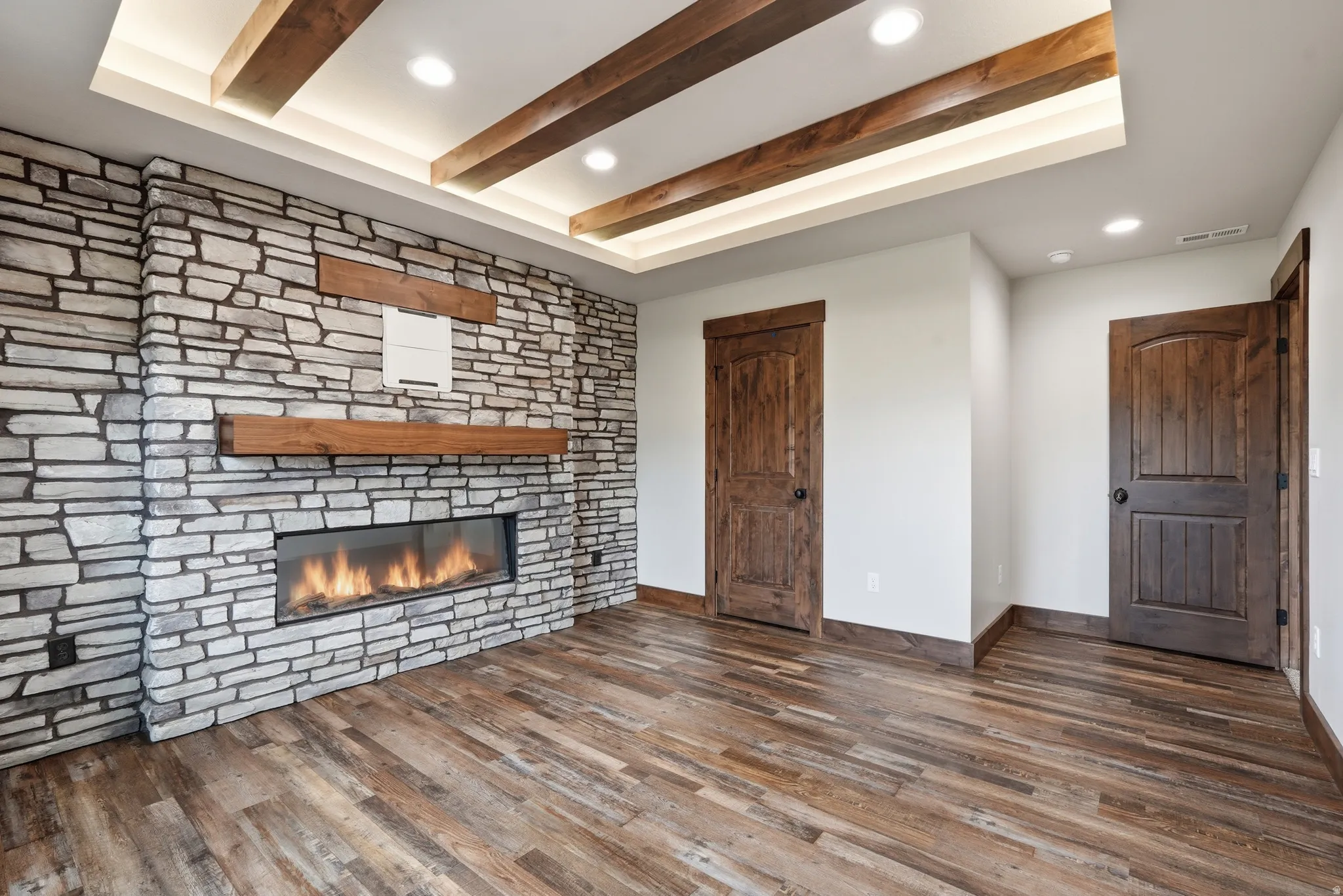 Unfurnished living room featuring recessed lighting, dark wood-style flooring, beamed ceiling, and a stone fireplace