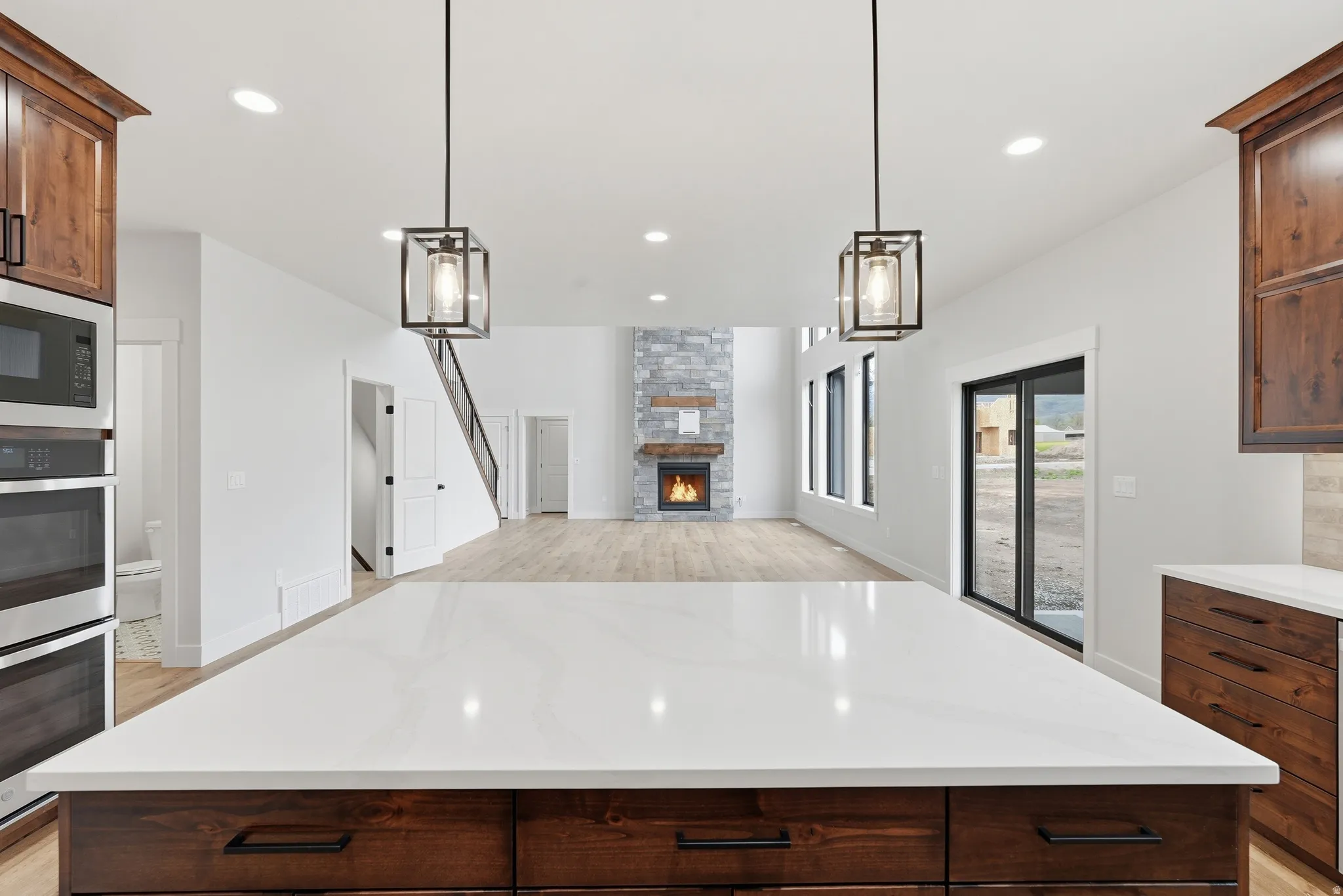 Kitchen with dark wood finish cabinetry, a stone fireplace, light stone countertops, open floor plan, and stainless steel appliances