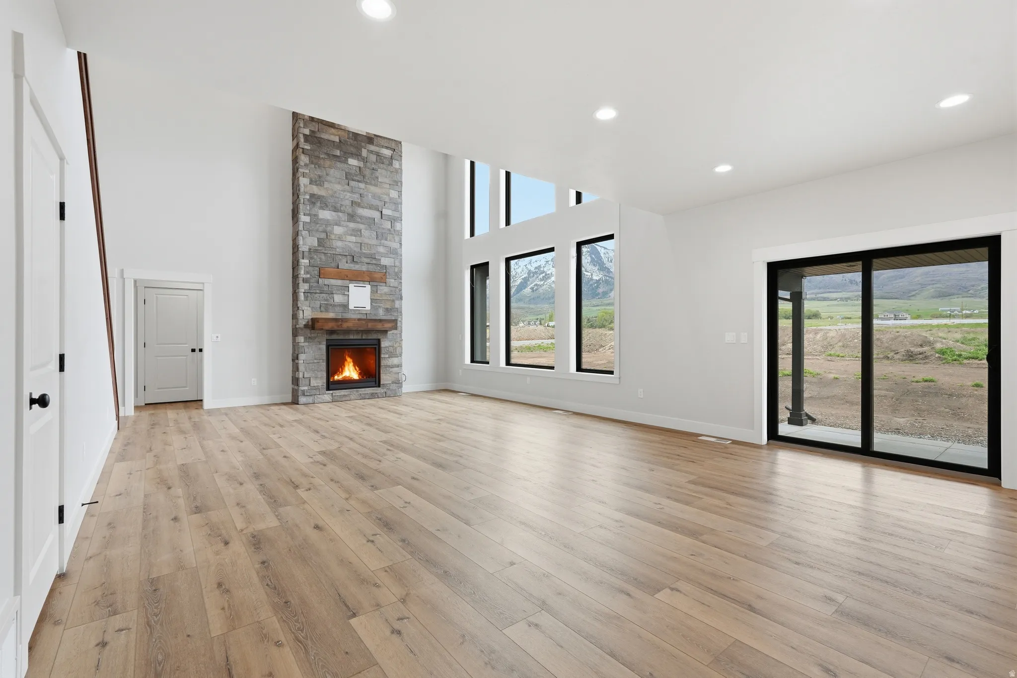 Unfurnished living room featuring a high ceiling, a fireplace, light wood finished floors, and recessed lighting