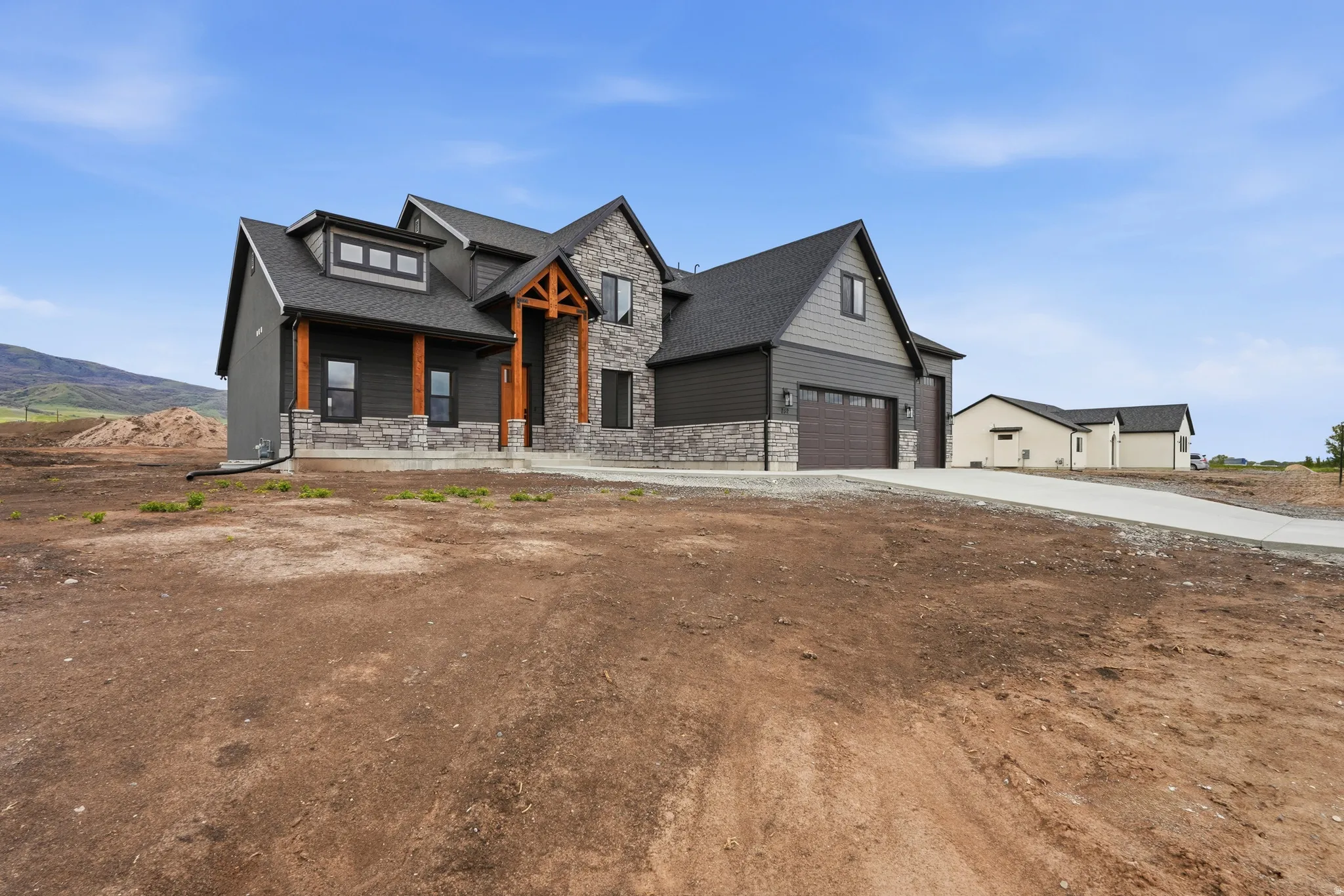 Modern farmhouse with stone siding, a garage, covered porch, roof with shingles, and driveway