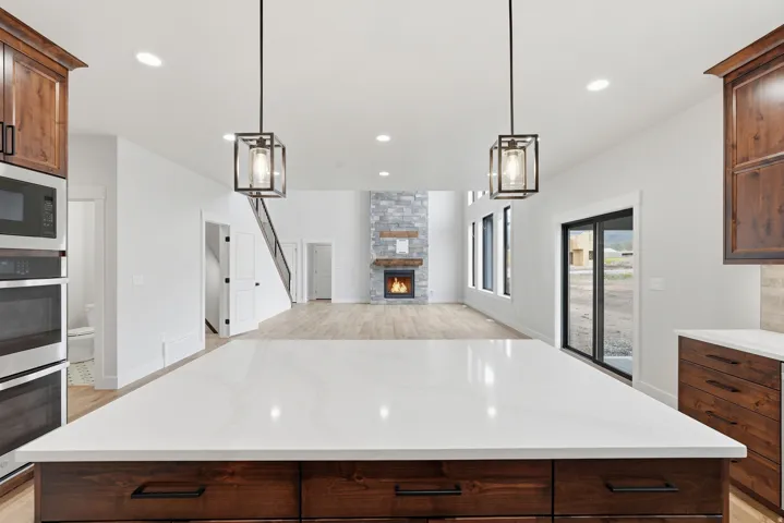 Kitchen with dark wood finish cabinetry, a stone fireplace, light stone countertops, open floor plan, and stainless steel appliances