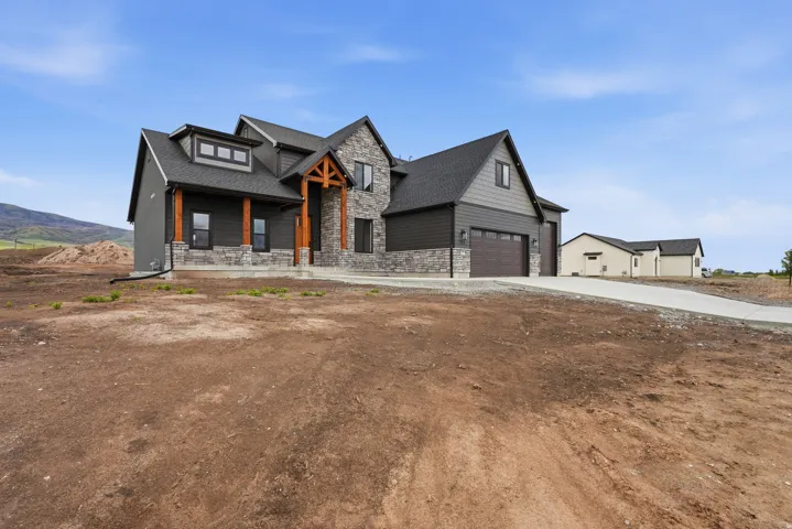 Modern farmhouse with stone siding, a garage, covered porch, roof with shingles, and driveway