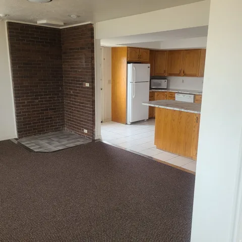 Kitchen featuring white appliances, light countertops, wood finish cabinetry, light colored carpet, and light tile patterned flooring