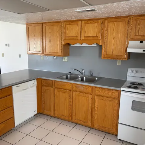 Kitchen with white appliances, wood finish cabinets, light tile patterned floors, and light countertops