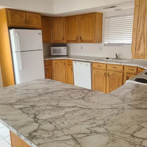 Kitchen with white appliances, wood finish cabinetry, and light countertops