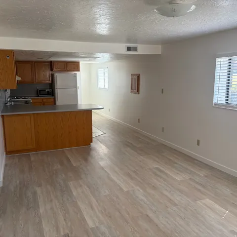 Kitchen with wood finish cabinets, a peninsula, freestanding refrigerator, a textured ceiling, and light wood-style floors