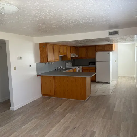 Kitchen with wood finish cabinetry, a peninsula, white appliances, a textured ceiling, and light wood-style flooring