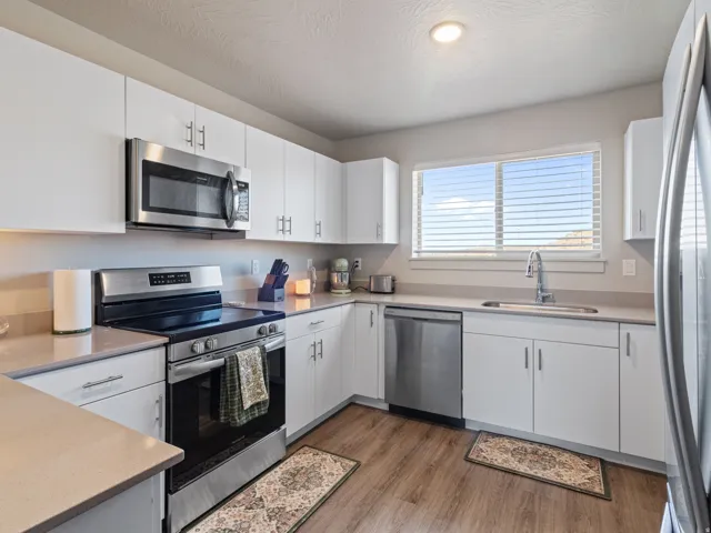 Kitchen with stainless steel appliances, white cabinets, light wood finished floors, and light stone countertops