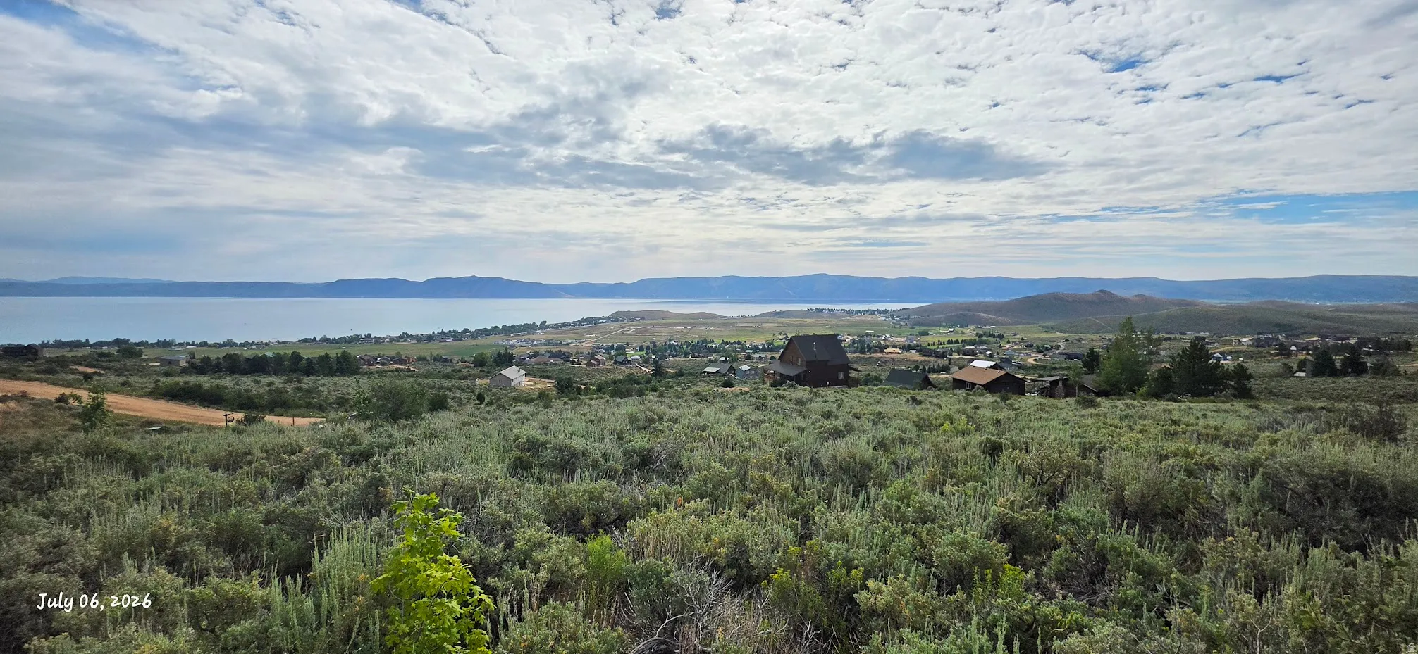 Expansive natural landscape featuring varied green foliage, distant water body, and surrounding hills