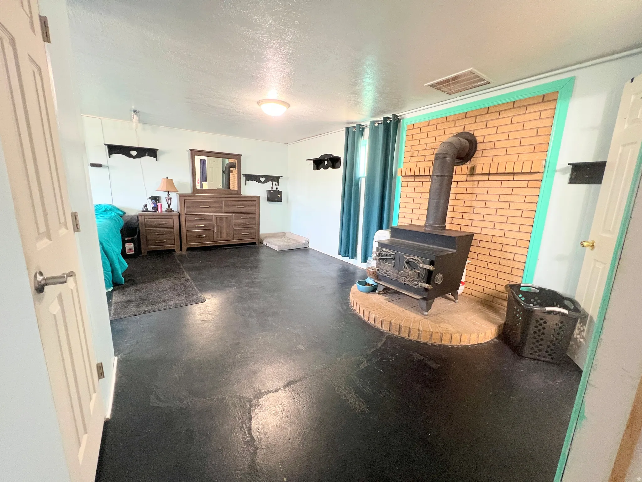 bedroom/living room featuring a textured ceiling, finished concrete flooring, and a wood stove