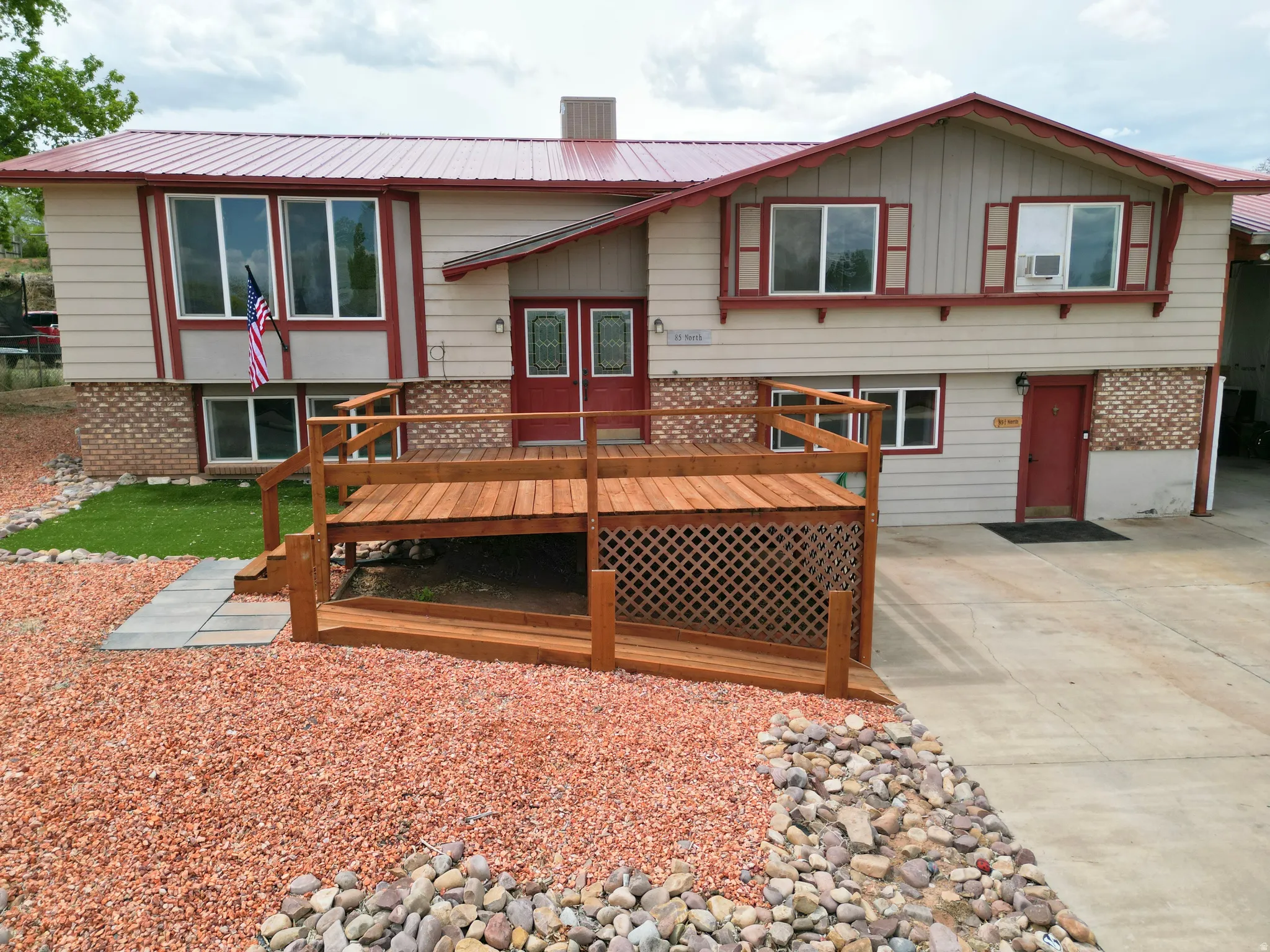 Back of house with a wooden deck, brick siding, a metal roof, board and batten siding, and driveway