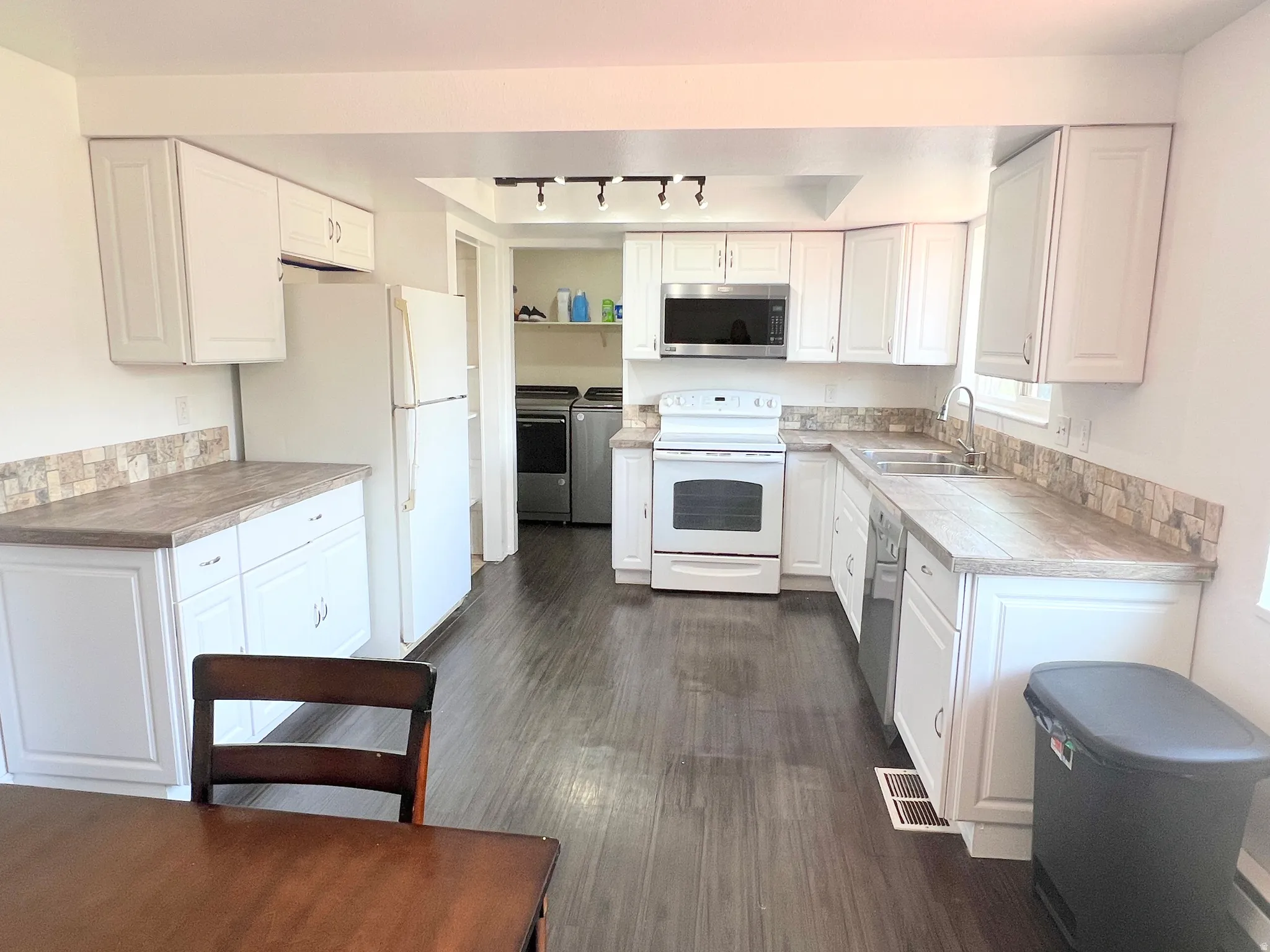 Kitchen featuring stainless steel appliances, white cabinets, independent washer and dryer, dark wood-style flooring, and track lighting