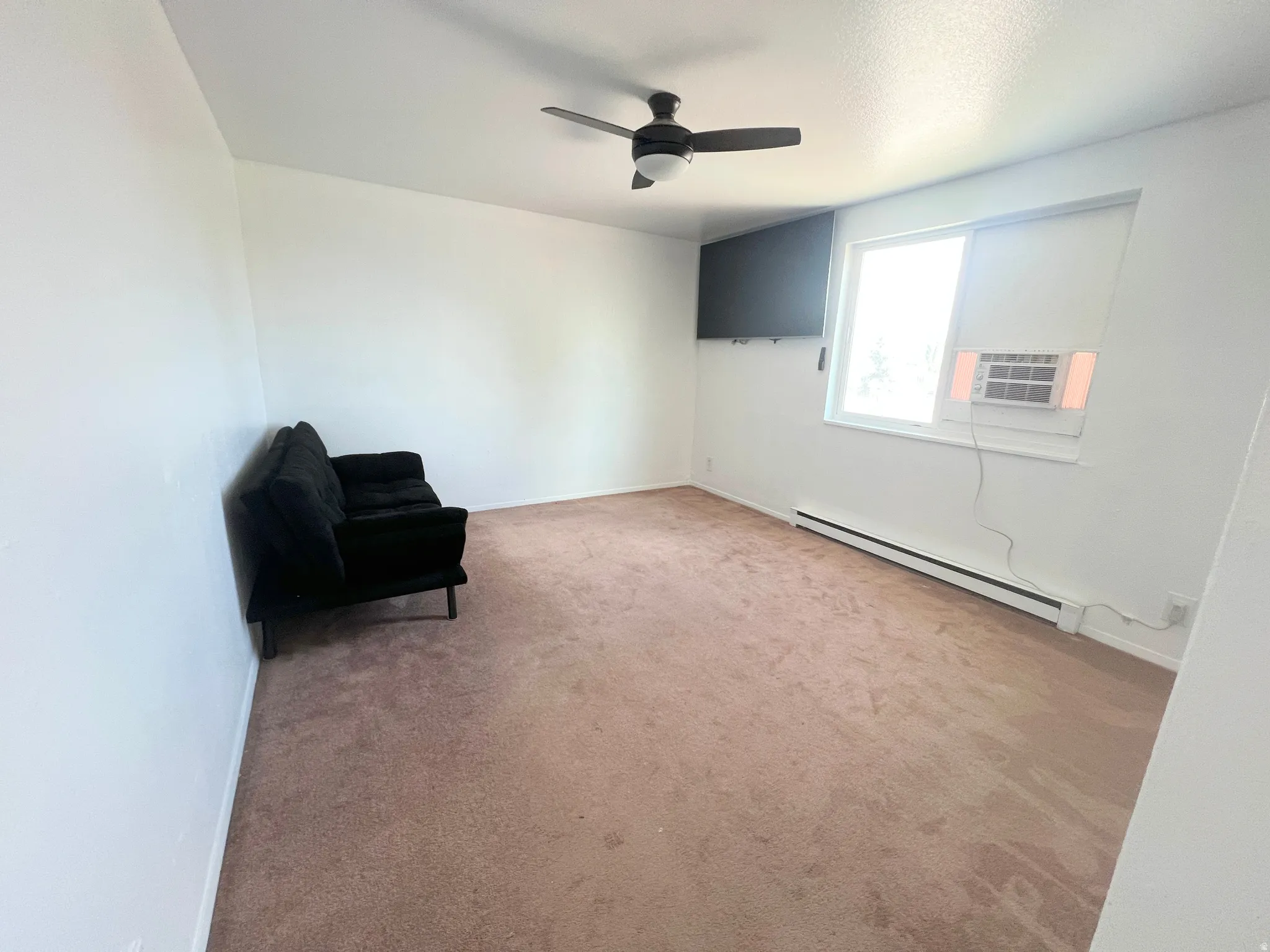 Unfurnished room featuring baseboard heating, carpet flooring, ceiling fan, and cooling unit