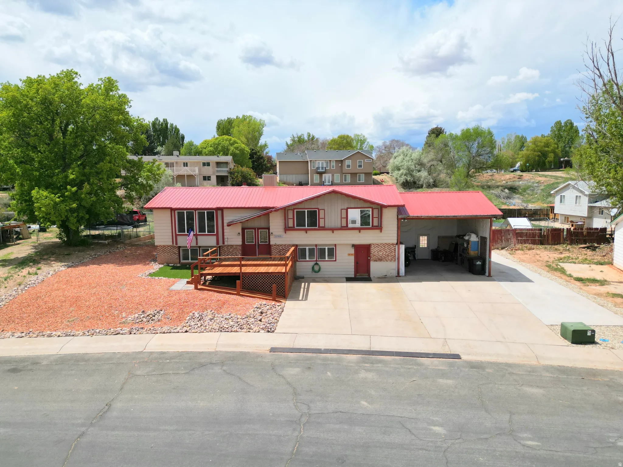 Raised ranch featuring a carport, a wooden deck, a metal roof, and driveway