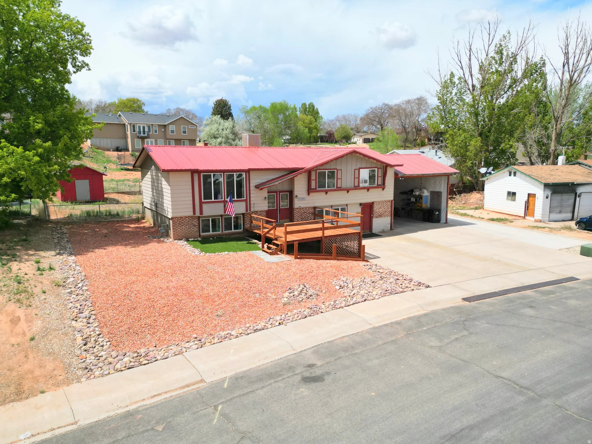 Bi-level home with a wooden deck, a metal roof, concrete driveway, an outbuilding, and an attached carport