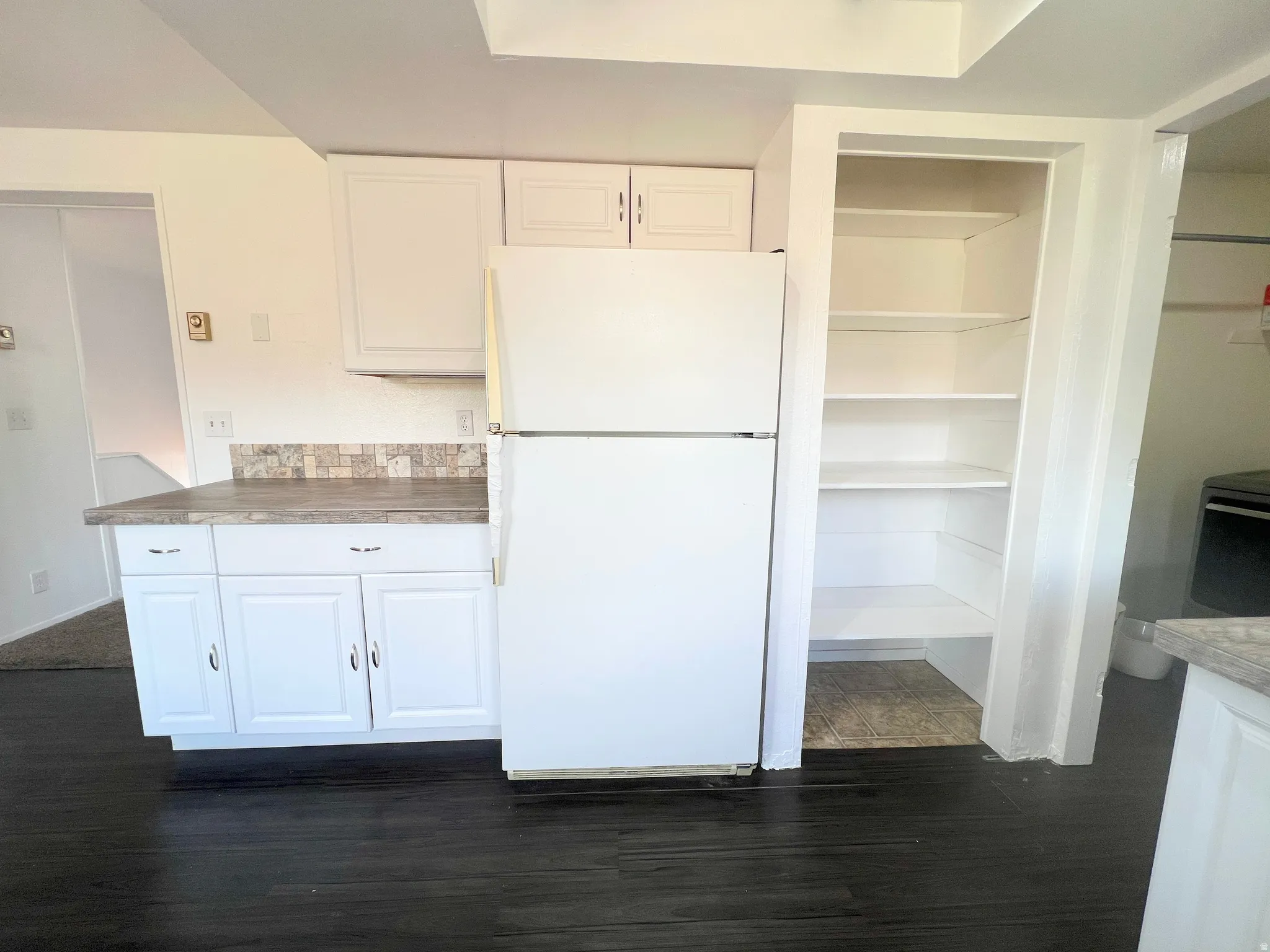 Kitchen featuring freestanding refrigerator, white cabinets, and dark wood-style flooring