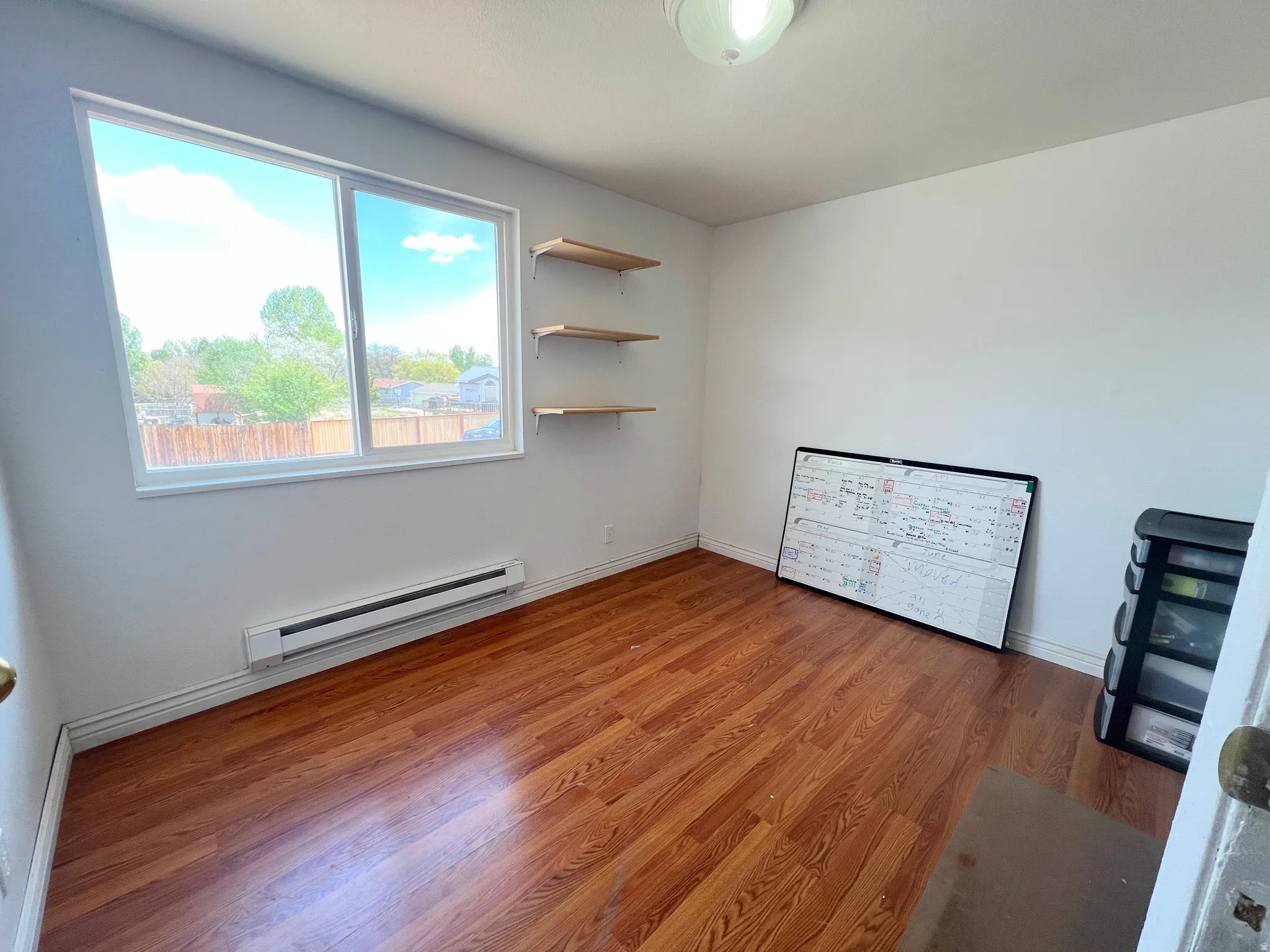 Unfurnished bedroom with a baseboard heating unit and wood finished floors
