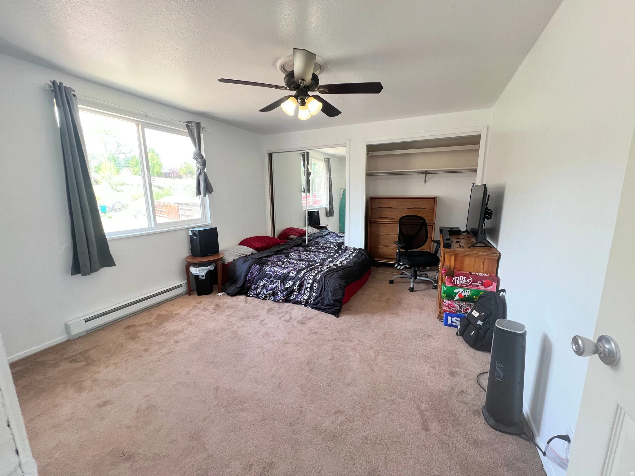 Bedroom with baseboard heating, ceiling fan, light carpet, two closets, and a desk