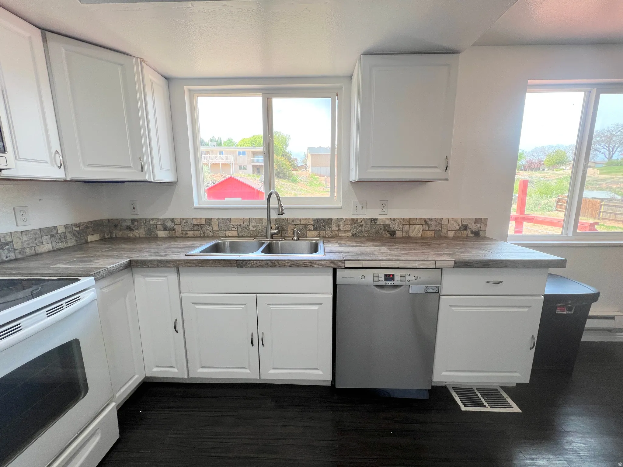Kitchen with electric range, white cabinetry, stainless steel dishwasher, and dark countertops