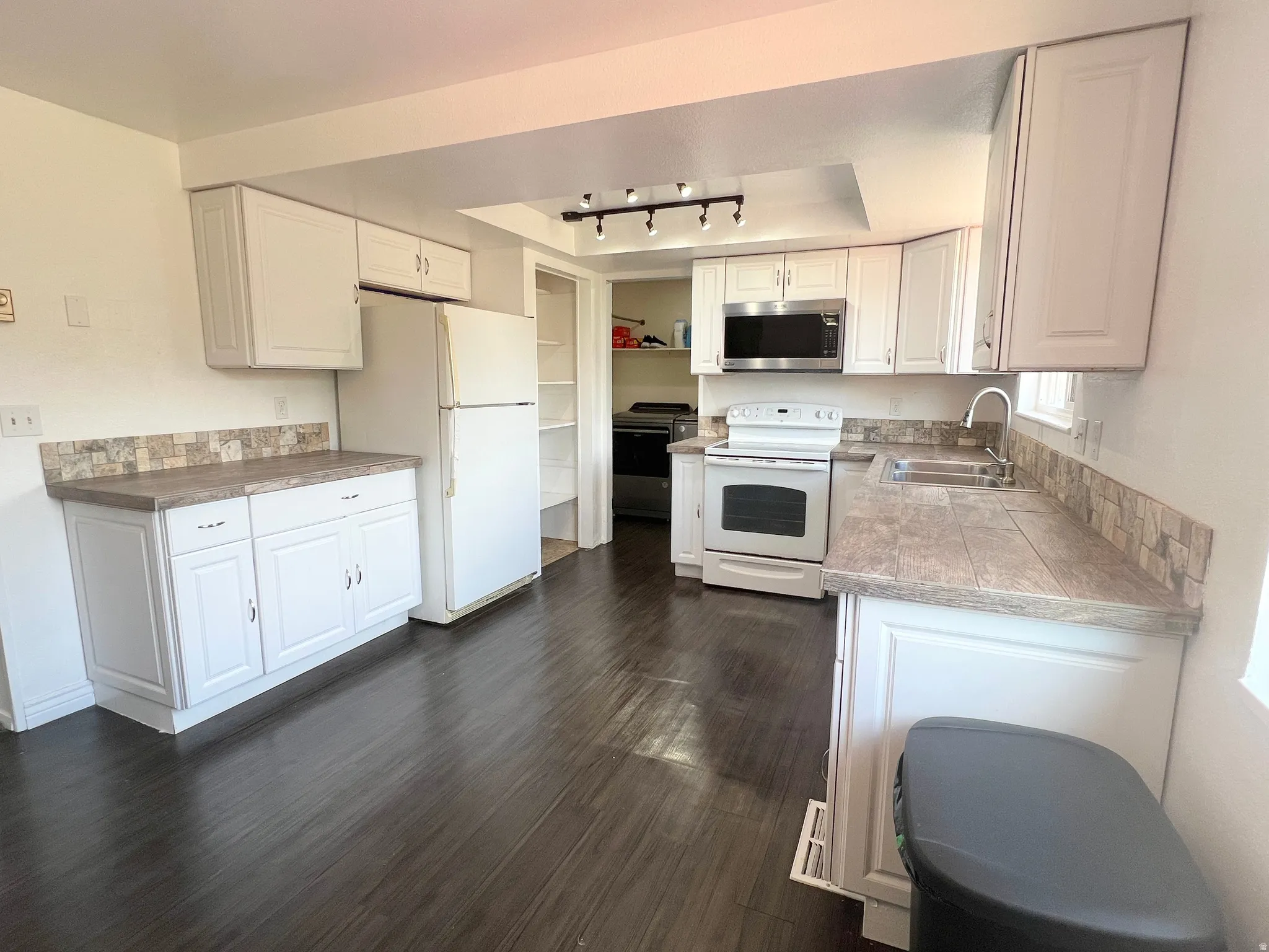 Kitchen featuring white appliances, white cabinets, dark wood-style flooring, tile countertops, and rail lighting