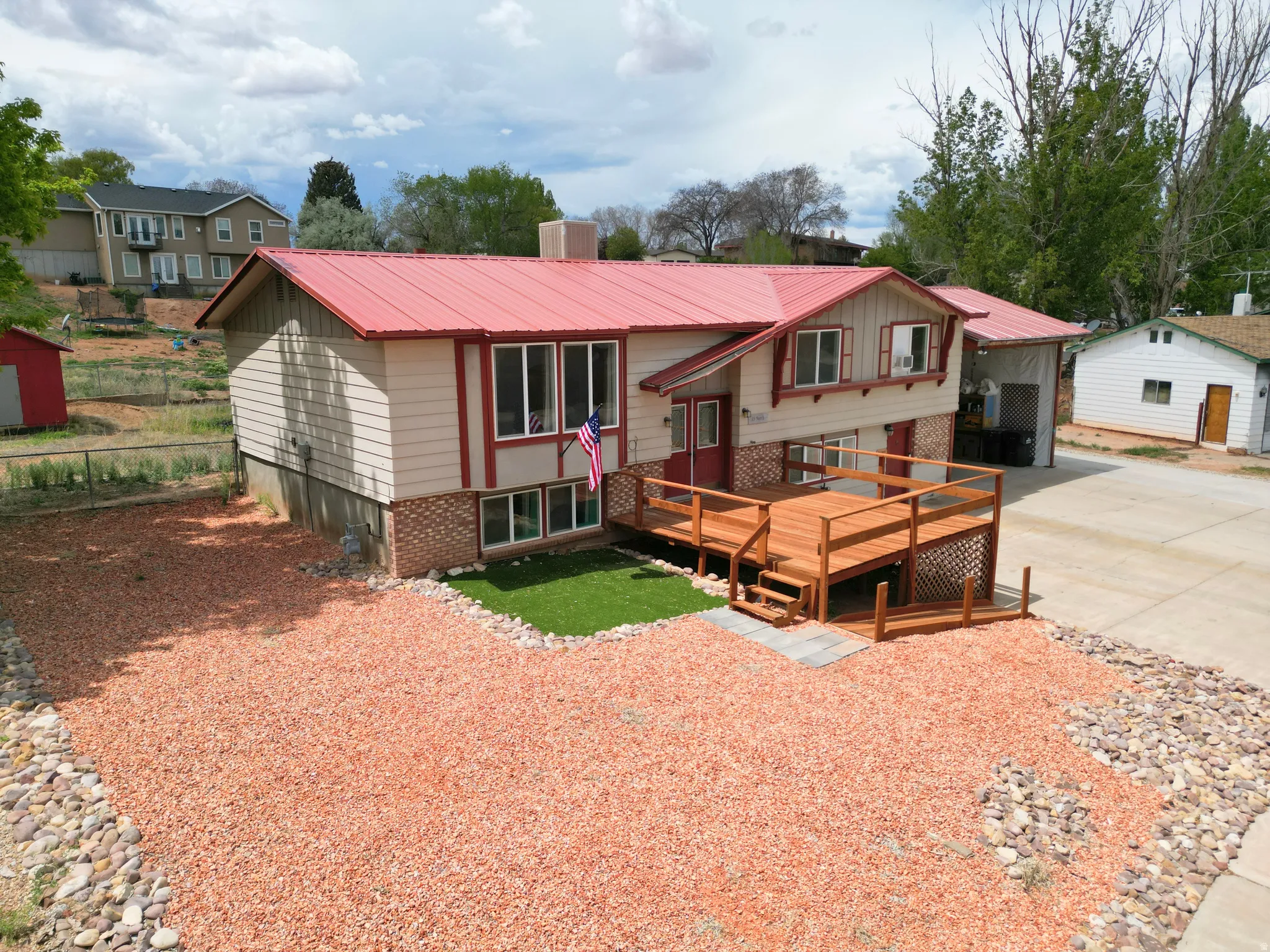 Bi-level home featuring a metal roof, a deck, concrete driveway, brick siding, and a chimney