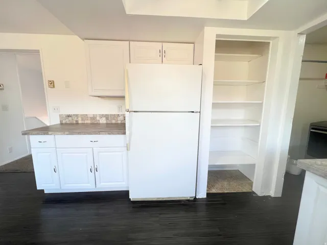 Kitchen featuring freestanding refrigerator, white cabinets, and dark wood-style flooring
