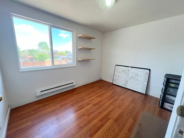 Unfurnished bedroom with a baseboard heating unit and wood finished floors