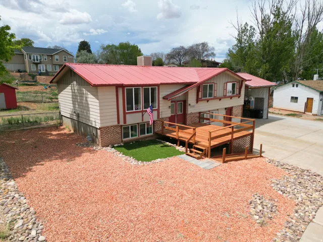 Bi-level home featuring a metal roof, a deck, concrete driveway, brick siding, and a chimney