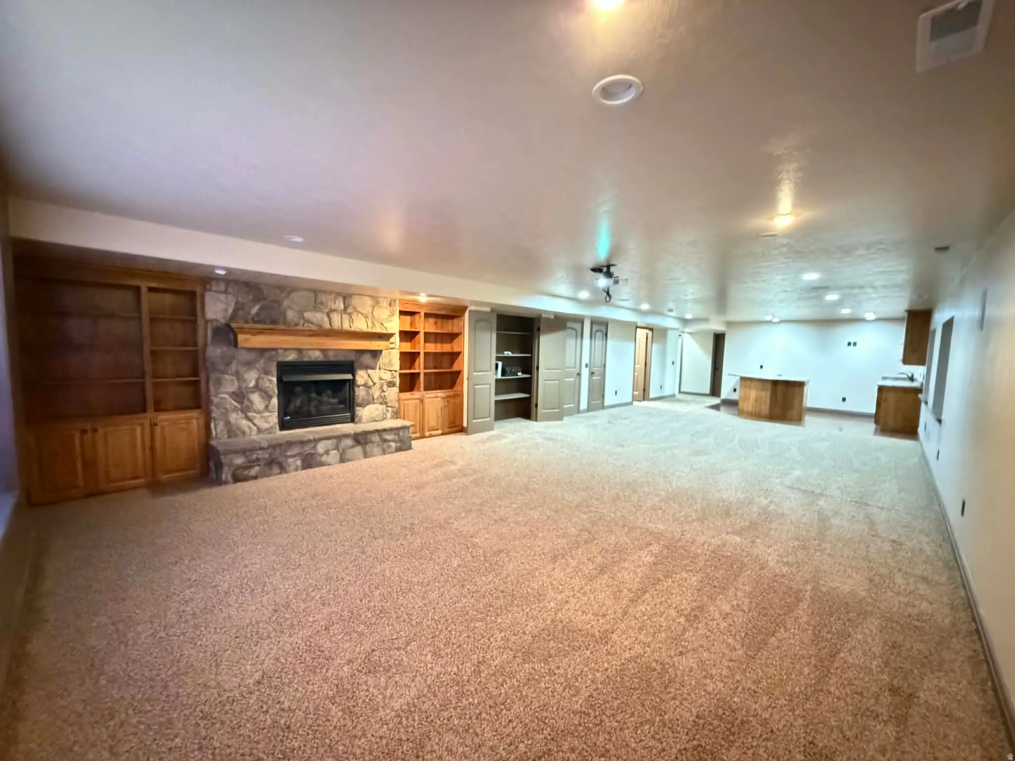 Unfurnished living room featuring a stone fireplace, carpet flooring, and built in shelves
