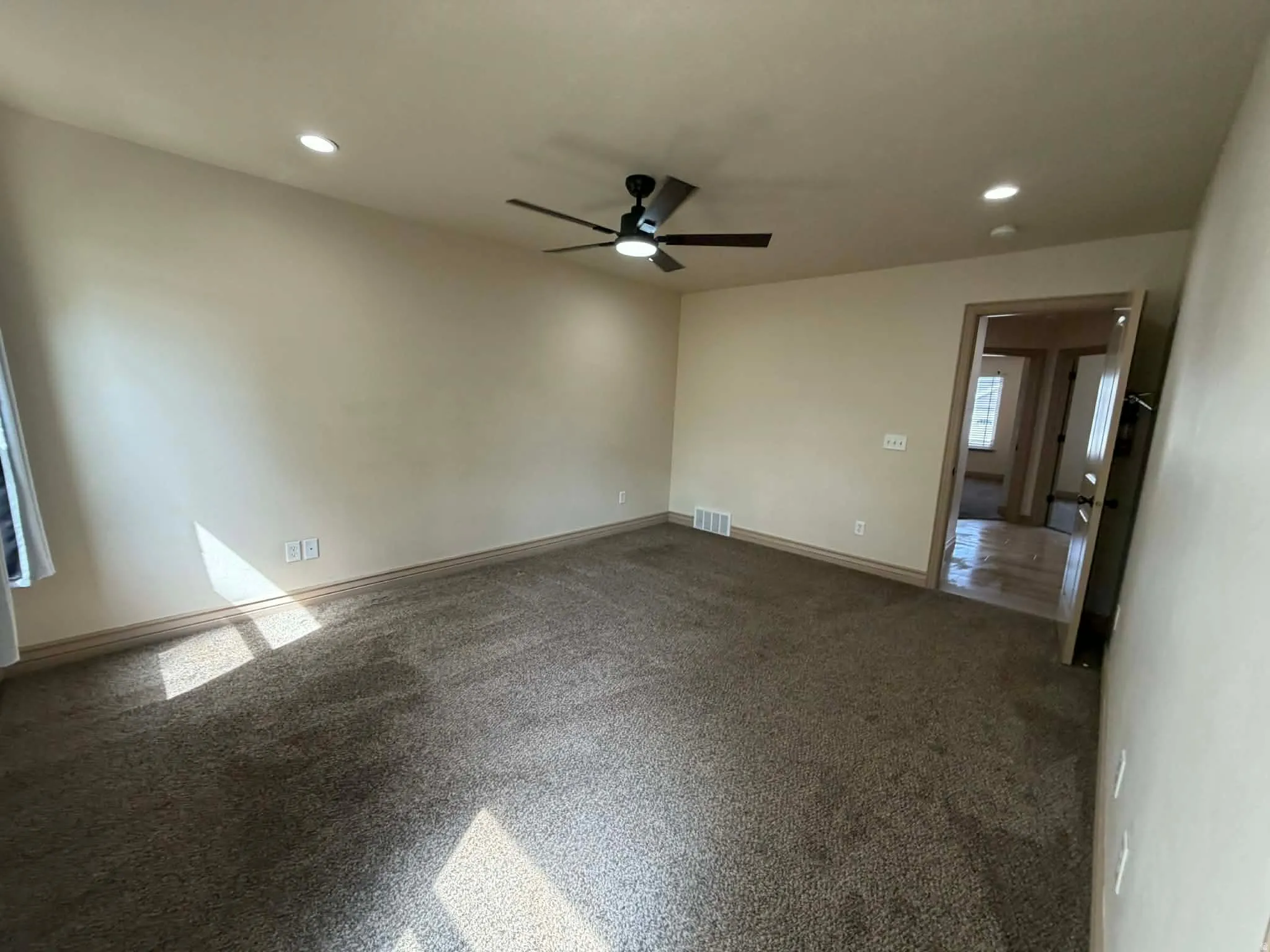 Empty room featuring dark carpet, ceiling fan, and recessed lighting