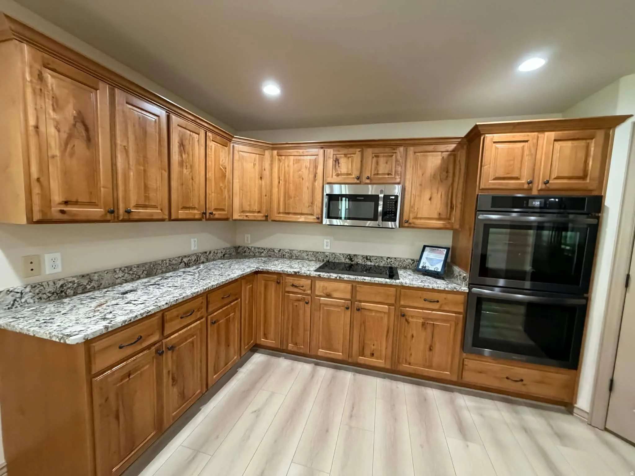 Kitchen with wood finish cabinetry, light stone counters, double oven, and recessed lighting