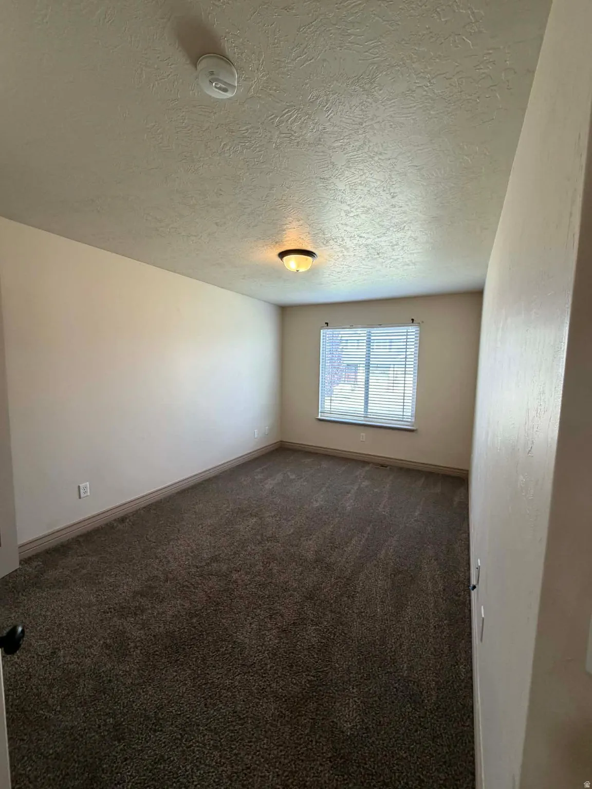 Spare room with dark carpet, a textured ceiling, and a smoke detector