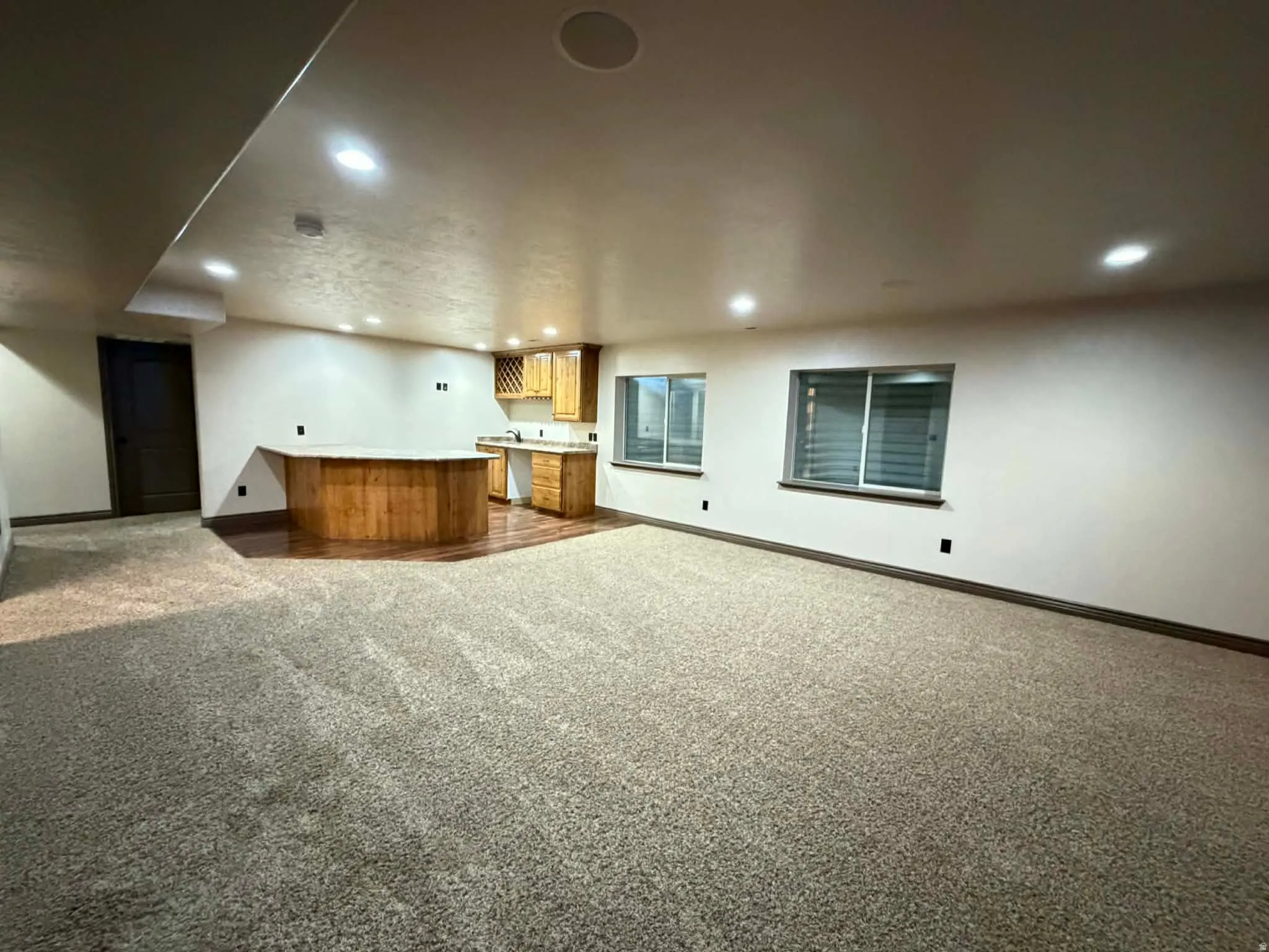 Indoor wet bar featuring dark carpet, light countertops, recessed lighting, and wood finish cabinetry