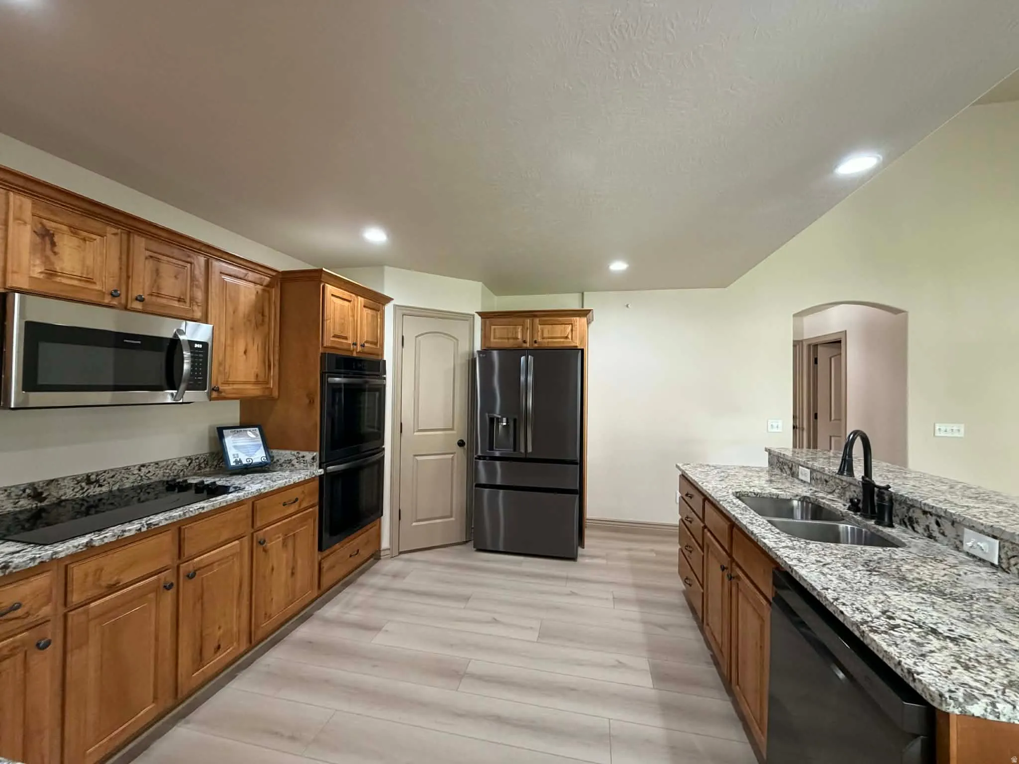 Kitchen featuring wood finish cabinetry, black appliances, light stone counters, and recessed lighting